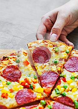 Woman Hand takes a slice of Pizza with vegetables mix, Mozzarella cheese, pepperoni, tomato, salami. Italian pizza on wooden table