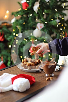 Woman hand taking christmas gingerbread cookie from plate and hot chocolate.