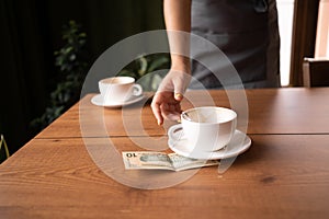 Woman hand taking cup wsth US dollar banknotes on cafe's table, two cups of tea on background. payment, service