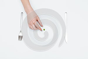 Woman hand taking one green pea from the plate