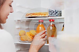 Woman hand taking, picks up juice glass bottle out of open refrigerator, fridge