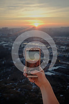 Woman hand taking picture of sunset landscape with smartphone from roof top