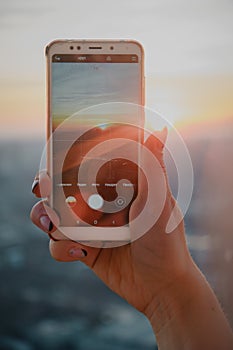 Woman hand taking picture of sunset landscape with smartphone from roof top