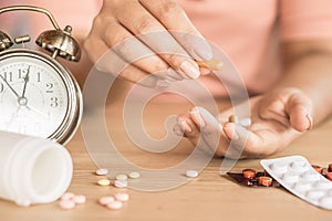 Woman hand taking pills with glass of water and clock on desk,