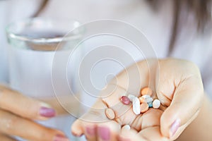 Woman hand taking vitamins another hand holding glass of water