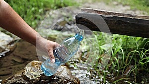 Woman hand taking water from forest spring on hiking trip. Hiker crouching on rocks, filling bottle up with cold