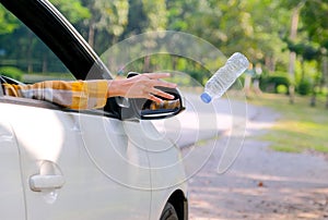Woman hand throw clear bottle with blue cap out from car window with the concept human garbage destroy environment photo