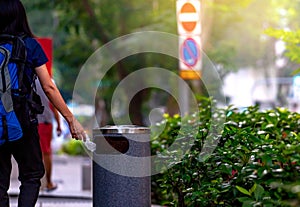 Woman hand throwing twisted empty water bottle in recycle bin. Gray plastic recycle bin. Backpacker discard bottle in trash bin.