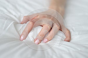 Woman hand tightly grips white sheet on bed