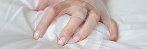 Woman hand tightly grips white sheet on bed