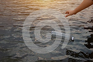 Woman hand to pick up the used waste plastic bottle on the water in a canal