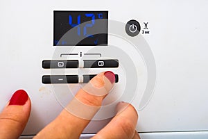 Woman hand try to turn off and on the central heating in the room. Female hands on the central heating control panel. Girl hand