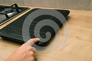 Woman hand turn on induction stove. Finger touching sensor button on induction or electrical hob. Modern kitchen appliance