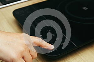 Woman hand turn on induction stove. Finger touching sensor button on induction or electrical hob. Modern kitchen appliance