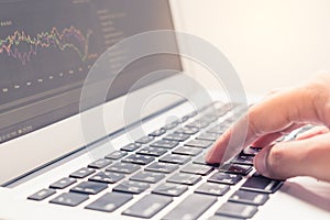 Woman hand typing on laptop keyboard with graph on screen