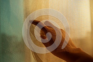Woman hand under net fabric point finger to the window with orange blue light background