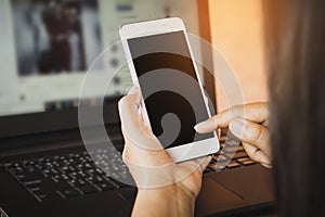 Woman hand using smart phone while working on laptop