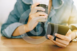 Woman hand using smartphone while drinking coffee with cafe shop colorful highlight shade to object beautiful backgroun