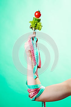 Woman hand with vegetarian food and measuring tapes.