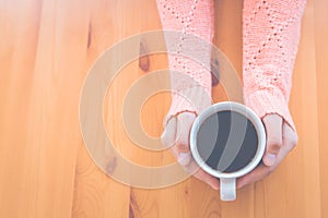 Woman hand in warm pink sweater holding a cup of coffee and hear