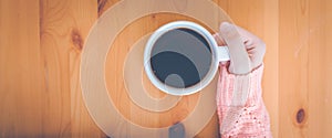 Woman hand in warm pink sweater holding a cup of coffee.Web banner