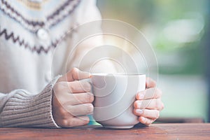 Woman hand in warm sweater holding a cup of coffee.