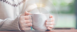 Woman hand in warm sweater holding a cup of coffee and smoke.Web banner.
