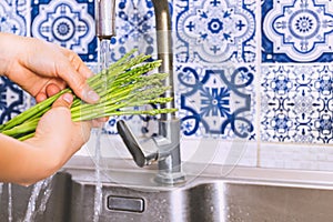 Woman hand washing green asparagus in kitchen sink.