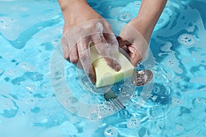 Woman hand washing spoon and fork in water