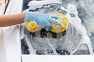 Woman hand wearing blue gloves with yellow sponge washing rear mirror modern car or cleaning automobile.