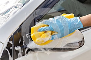Woman hand wearing blue gloves with yellow sponge washing side mirror modern car or cleaning automobile.