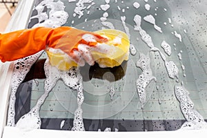 Woman hand wearing orange gloves with yellow sponge washing rear mirror modern car or cleaning automobile.