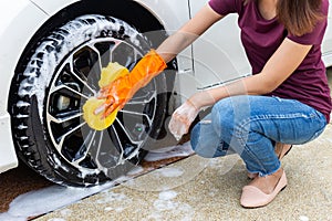 Woman hand wearing orange gloves with yellow sponge washing wheel modern car or cleaning automobile.