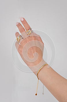 Woman hand wearing Snake Chain bracelets and Interlocked Golden and Silver Rings set against a white background. Beautiful