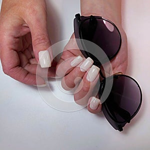 A woman hand with a white manicure holds sunglasses