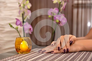 Woman hand with wine color nails polish on a desk and candle decoration on a desk