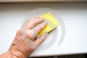 Woman hand wiping dust from a window sill with a sponge, cleaning and tiding up the house every day