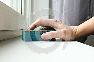 Woman hand wiping dust from a window sill with a sponge, cleaning and tiding up the house every day