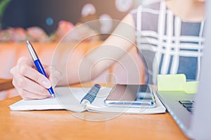 Woman hand working at a computer and writing on a notepad with a pen in the office