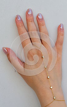 Woman hand wrist wearing golden hand chain set against a white background