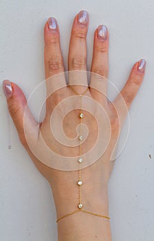 Woman hand wrist wearing golden hand chain set against a white background