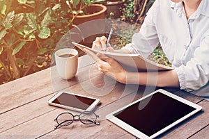 Woman hand writing book and phone, tablet on table in garden at