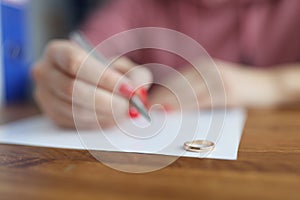 Woman hand writing declaration of divorce on background of wedding rings closeup