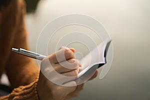 Woman hand writing down in small white memo notebook.