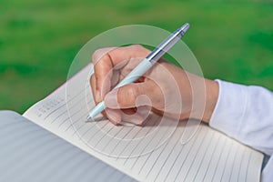Woman hand writing down in small white memo notebook for take a note not to forget or to do list plan