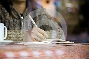 Woman hand writing on notebook in the cafe in rainy day