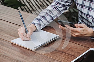 Woman hand writing notepad and holding phone on wooden table at coffee shop