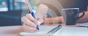 Woman hand is writing on a notepad with a pen in office.Web banner