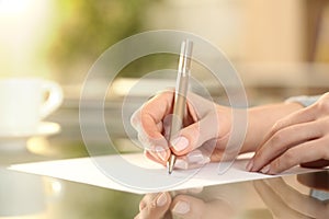 Woman hand writing on a paper on a desk at home