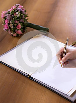 Woman hand writing with pen in book with textspace copyspace wedding flower bouquet